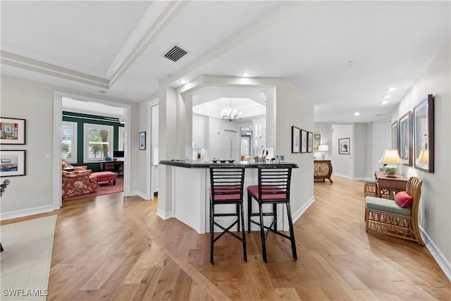 kitchen with light hardwood / wood-style floors, a raised ceiling, a breakfast bar area, and an inviting chandelier