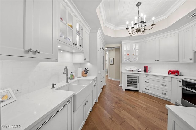 kitchen with oven, light hardwood / wood-style floors, white cabinets, pendant lighting, and beverage cooler