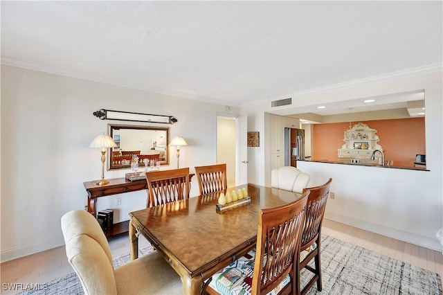 dining room with crown molding, sink, and light wood-type flooring