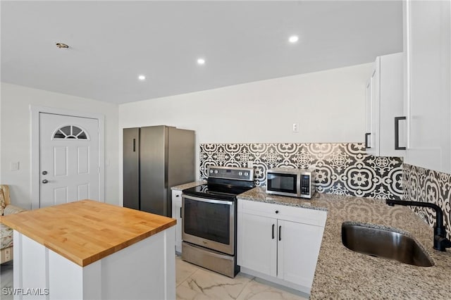 kitchen with butcher block counters, decorative backsplash, marble finish floor, stainless steel appliances, and a sink