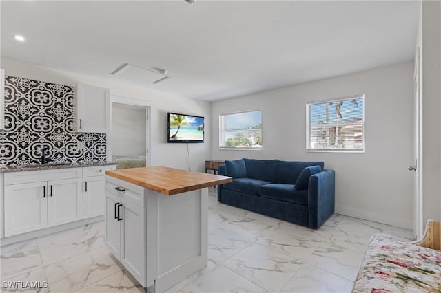 kitchen with butcher block countertops, marble finish floor, open floor plan, white cabinetry, and baseboards