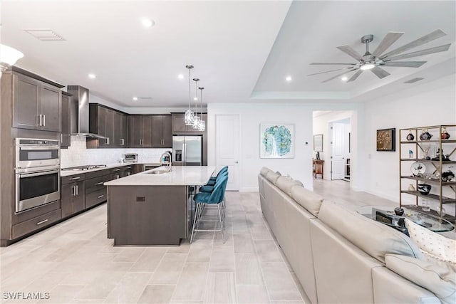 kitchen featuring open floor plan, stainless steel appliances, a sink, visible vents, and wall chimney exhaust hood