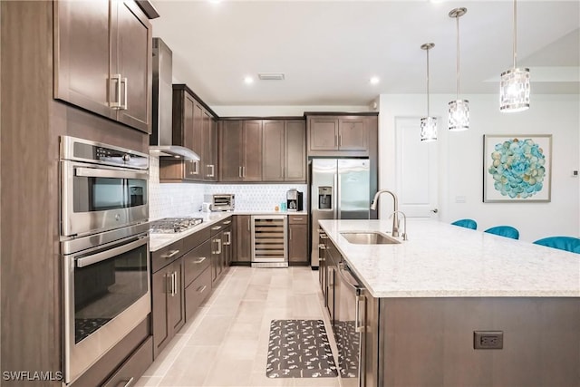 kitchen with wine cooler, dark brown cabinetry, a sink, appliances with stainless steel finishes, and a center island with sink