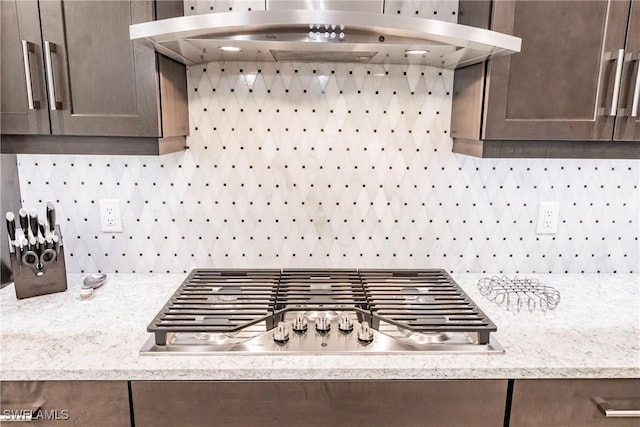 room details featuring stainless steel gas stovetop, light stone countertops, tasteful backsplash, dark brown cabinetry, and exhaust hood