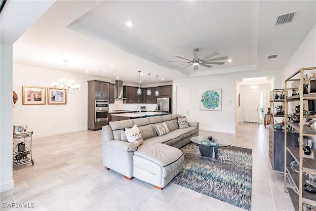 living area with ceiling fan with notable chandelier, recessed lighting, a tray ceiling, and visible vents