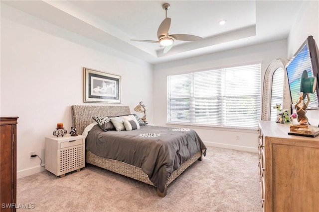 bedroom featuring a ceiling fan, a tray ceiling, baseboards, and light colored carpet