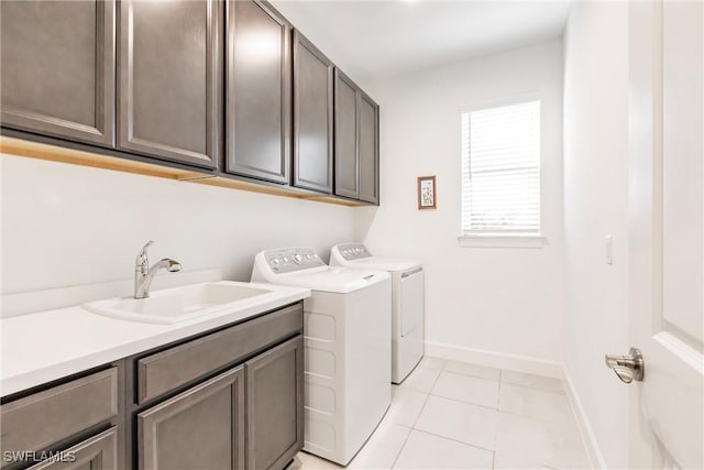clothes washing area featuring a sink, light tile patterned floors, baseboards, washer and dryer, and cabinet space