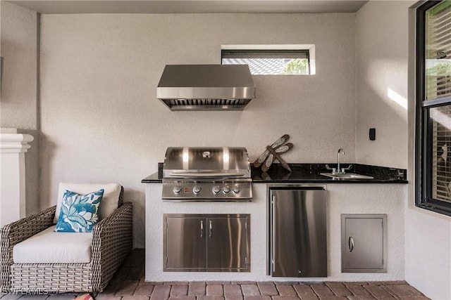 kitchen with wall chimney range hood, fridge, dark countertops, and a sink