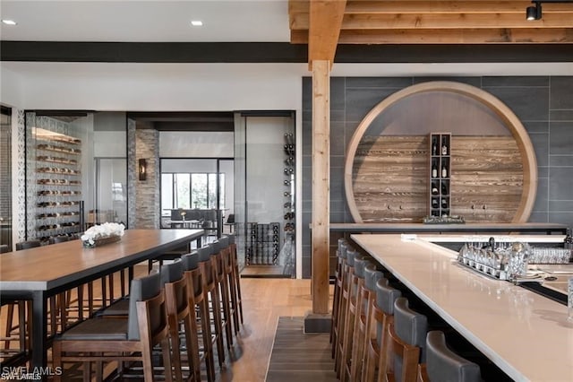 interior space with bar area, beam ceiling, and wood finished floors