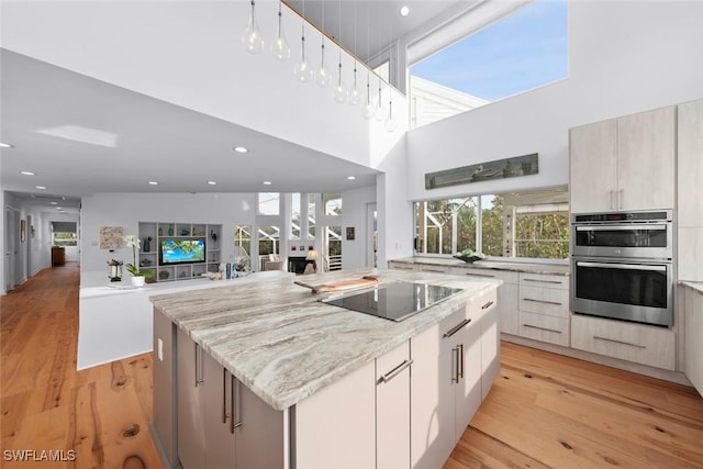 kitchen with a kitchen island, black electric stovetop, light stone countertops, stainless steel double oven, and light wood-type flooring