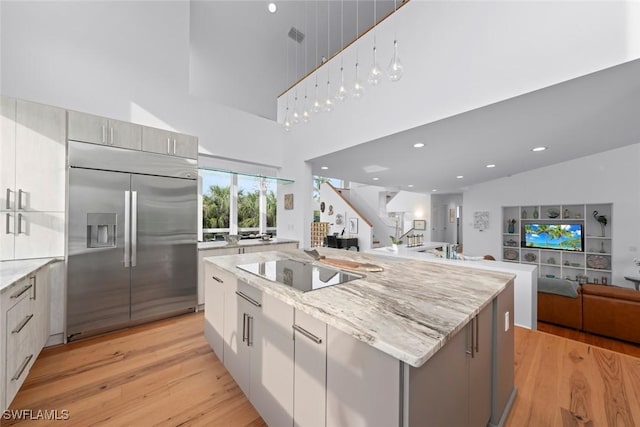 kitchen with built in fridge, light stone countertops, black electric stovetop, and a spacious island