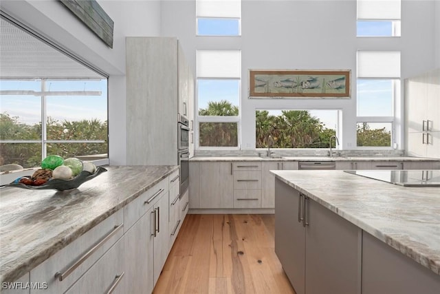 kitchen featuring light stone countertops, plenty of natural light, black electric stovetop, and light hardwood / wood-style flooring