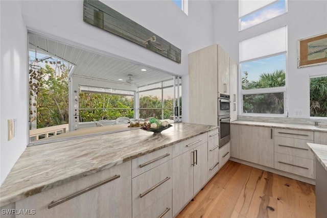 kitchen with light hardwood / wood-style flooring, light stone countertops, stainless steel double oven, and light brown cabinets