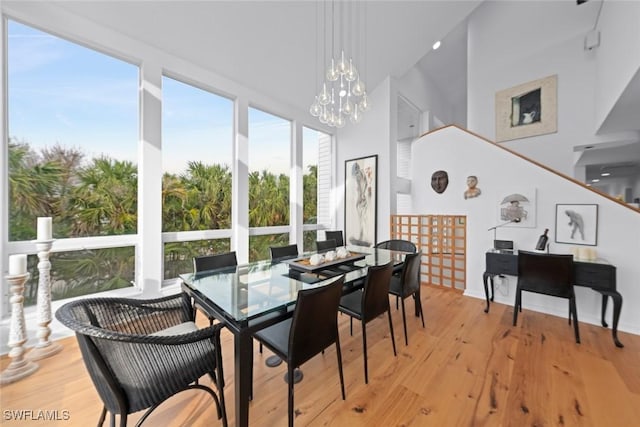 dining area with a notable chandelier, a towering ceiling, and light hardwood / wood-style flooring