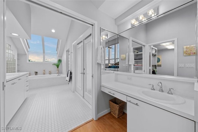 bathroom featuring vanity, tiled tub, vaulted ceiling, and wood-type flooring