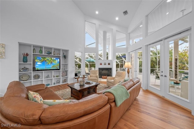 living room featuring high vaulted ceiling, light hardwood / wood-style floors, and french doors