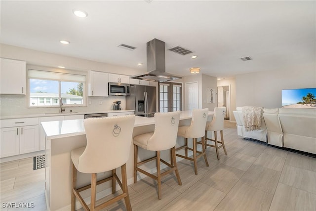 kitchen with stainless steel appliances, a center island, white cabinets, and island exhaust hood