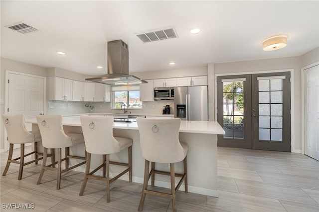 kitchen with appliances with stainless steel finishes, white cabinetry, a kitchen breakfast bar, a center island, and island range hood