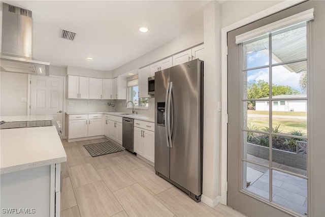 kitchen with white cabinets, appliances with stainless steel finishes, plenty of natural light, and island range hood