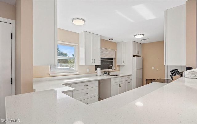 kitchen with white cabinetry, sink, light stone counters, and white fridge