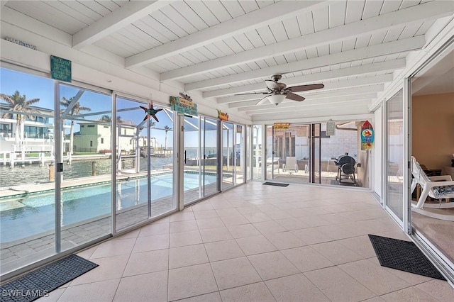 unfurnished sunroom featuring beam ceiling, a wealth of natural light, ceiling fan, and a water view