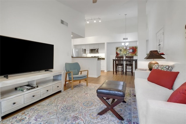 living room featuring an inviting chandelier, a towering ceiling, and light hardwood / wood-style flooring