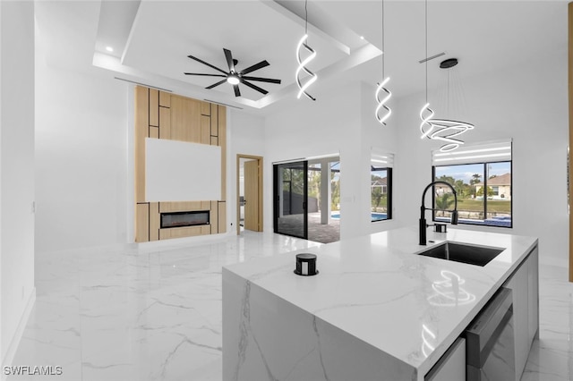 kitchen with a tray ceiling, a kitchen island with sink, light stone countertops, pendant lighting, and sink