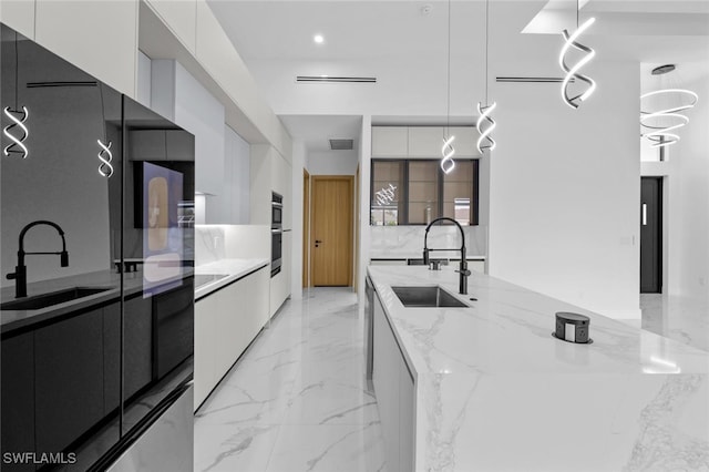 kitchen featuring hanging light fixtures, light stone countertops, sink, and white cabinetry