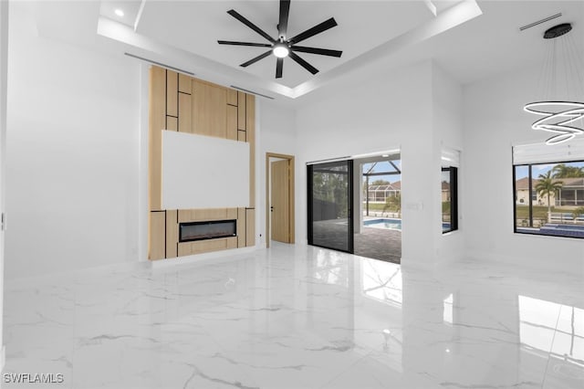 unfurnished living room featuring ceiling fan, a tile fireplace, and a tray ceiling