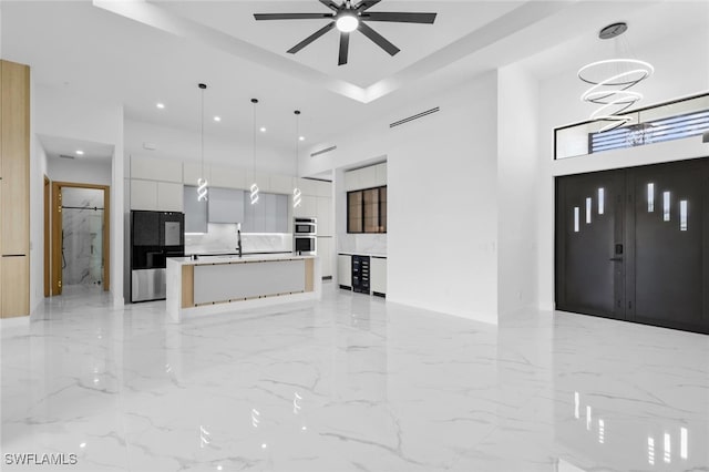 living room with a high ceiling, sink, and ceiling fan with notable chandelier