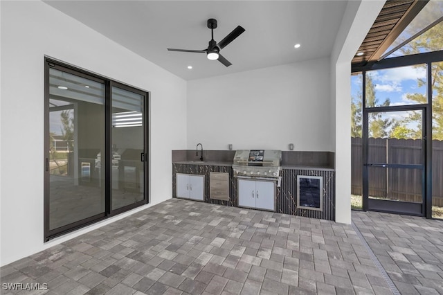 view of patio with grilling area, glass enclosure, ceiling fan, an outdoor kitchen, and sink