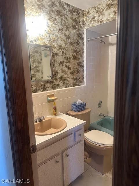 full bathroom with tile patterned floors, toilet, tiled shower / bath, tile walls, and vanity