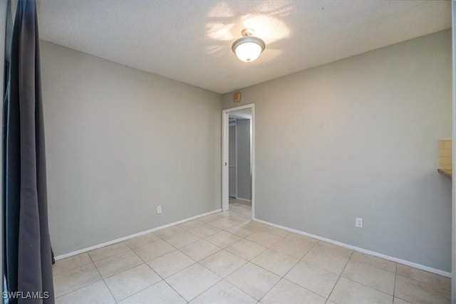 empty room featuring light tile patterned floors, a textured ceiling, and baseboards