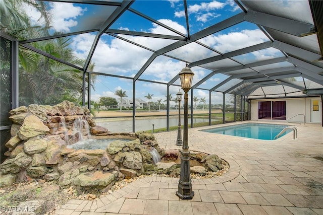 view of swimming pool with pool water feature, a water view, a patio area, and glass enclosure