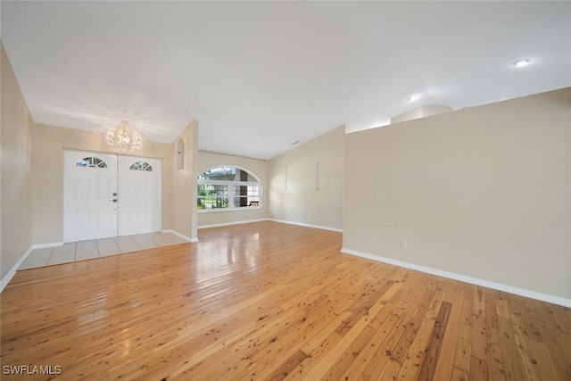 unfurnished living room with lofted ceiling, a notable chandelier, and light hardwood / wood-style floors