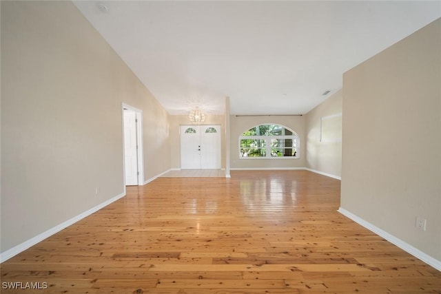 unfurnished living room featuring vaulted ceiling, light hardwood / wood-style flooring, and a notable chandelier