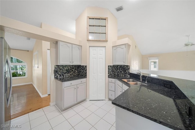 kitchen featuring light tile patterned floors, stainless steel fridge, backsplash, dark stone countertops, and sink