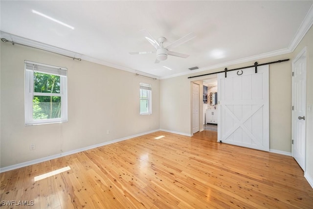 unfurnished bedroom with ceiling fan, a barn door, crown molding, and light hardwood / wood-style floors