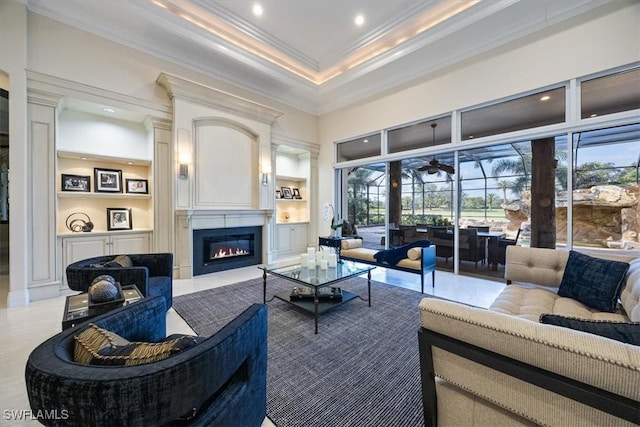 living room with a large fireplace, built in features, crown molding, and a towering ceiling