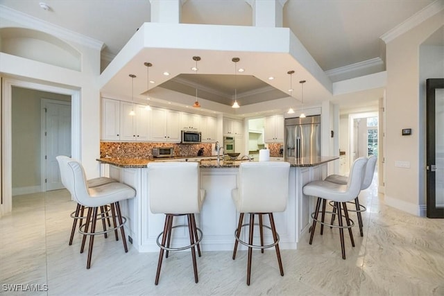 kitchen featuring appliances with stainless steel finishes, white cabinetry, pendant lighting, dark stone counters, and a tray ceiling