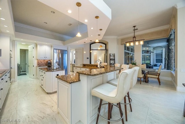 kitchen with hanging light fixtures, a spacious island, white cabinetry, dark stone counters, and built in fridge