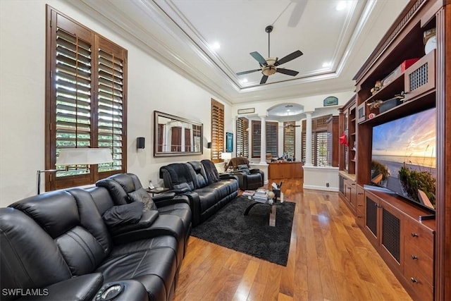 living room featuring plenty of natural light, ornamental molding, a raised ceiling, light wood-type flooring, and decorative columns