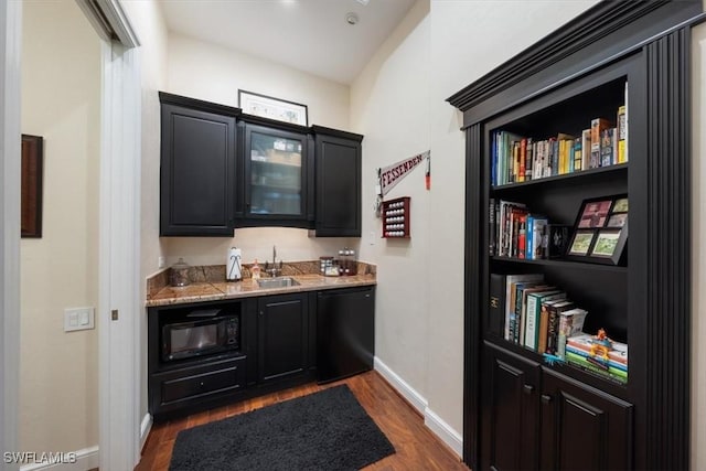 bar featuring light stone counters, sink, black appliances, and dark hardwood / wood-style flooring