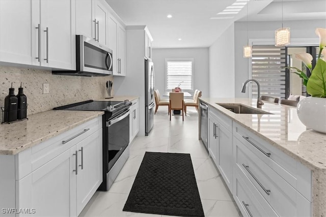 kitchen with sink, light stone counters, appliances with stainless steel finishes, pendant lighting, and white cabinets