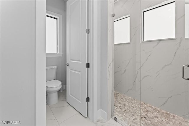 bathroom featuring a shower with door, toilet, and a healthy amount of sunlight