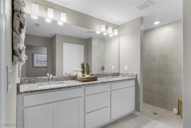 bathroom featuring a tile shower, a textured ceiling, tile patterned floors, and vanity