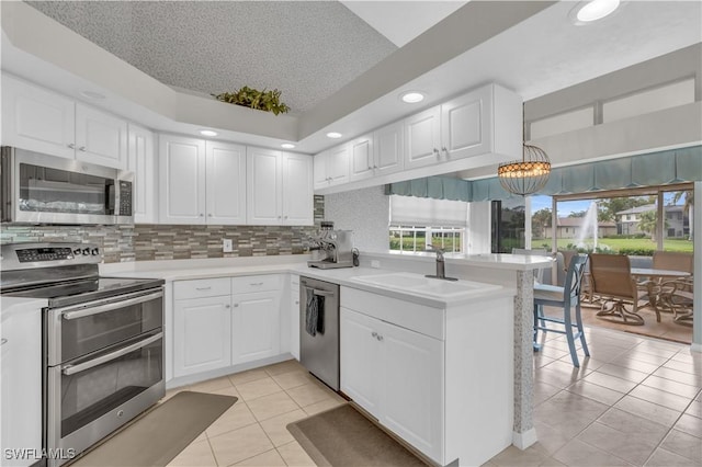 kitchen with kitchen peninsula, stainless steel appliances, white cabinetry, and hanging light fixtures