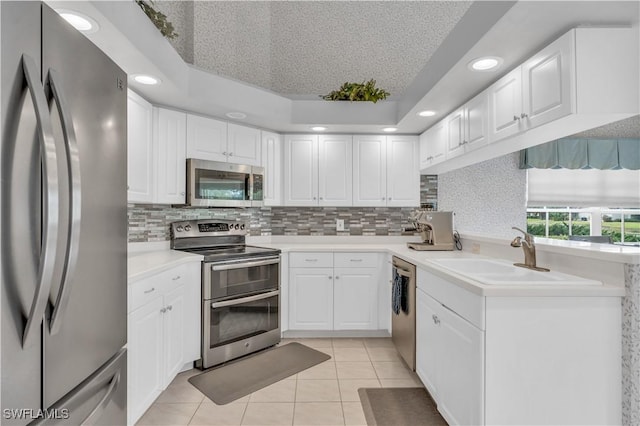 kitchen with appliances with stainless steel finishes, white cabinetry, sink, backsplash, and light tile patterned flooring