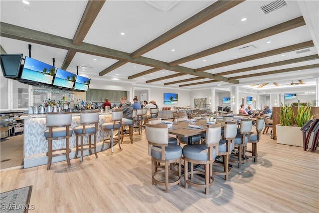 dining space featuring bar, coffered ceiling, light hardwood / wood-style flooring, and beamed ceiling