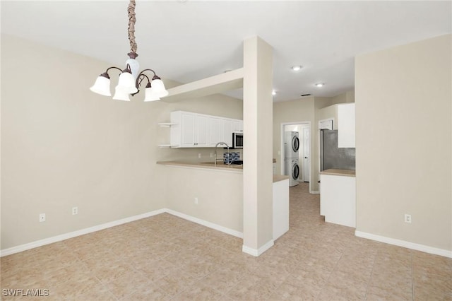 kitchen with white cabinetry, kitchen peninsula, decorative light fixtures, stacked washing maching and dryer, and a chandelier